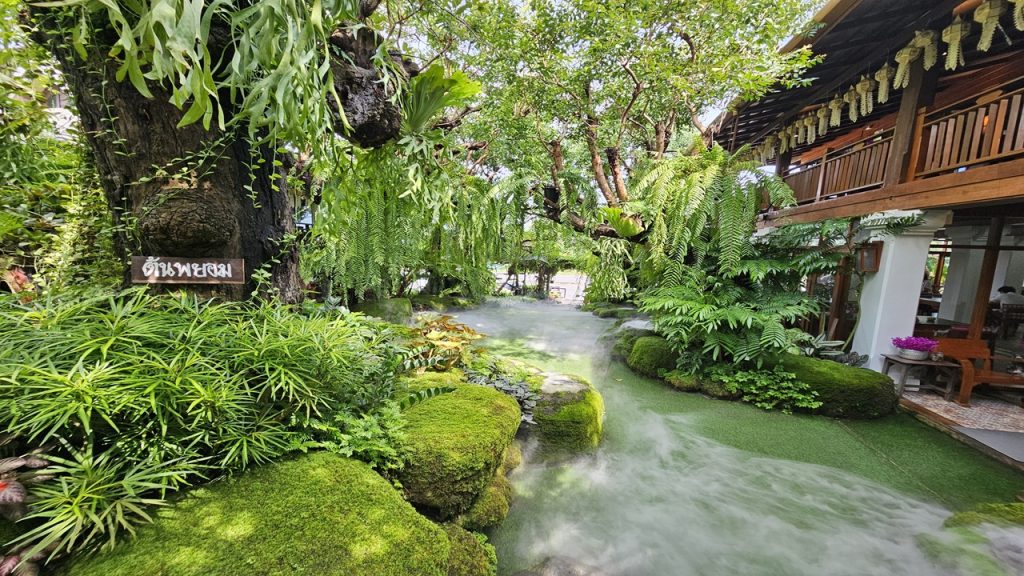 A lush green garden with moss-covered stones, ferns, and mist among tropical plants and traditional wooden architecture—a symbol of organic growth and holistic connectedness in Gestalt therapy