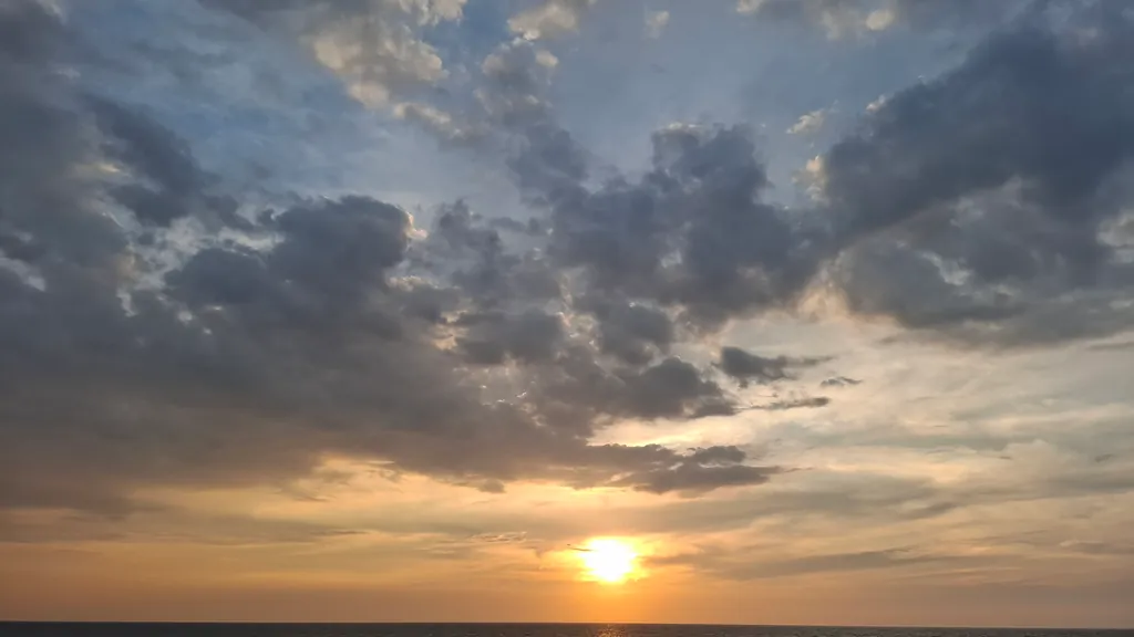Abendsonne zwischen Wolken knapp über dem Meer