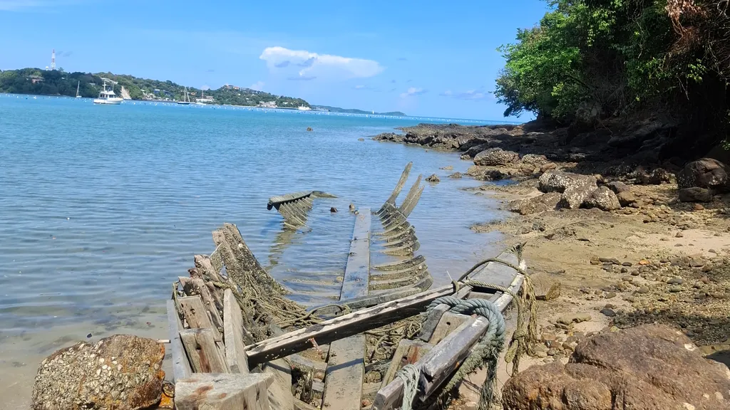 Wrack eines Holzboots am felsigen Ufer, dahinter das Meer