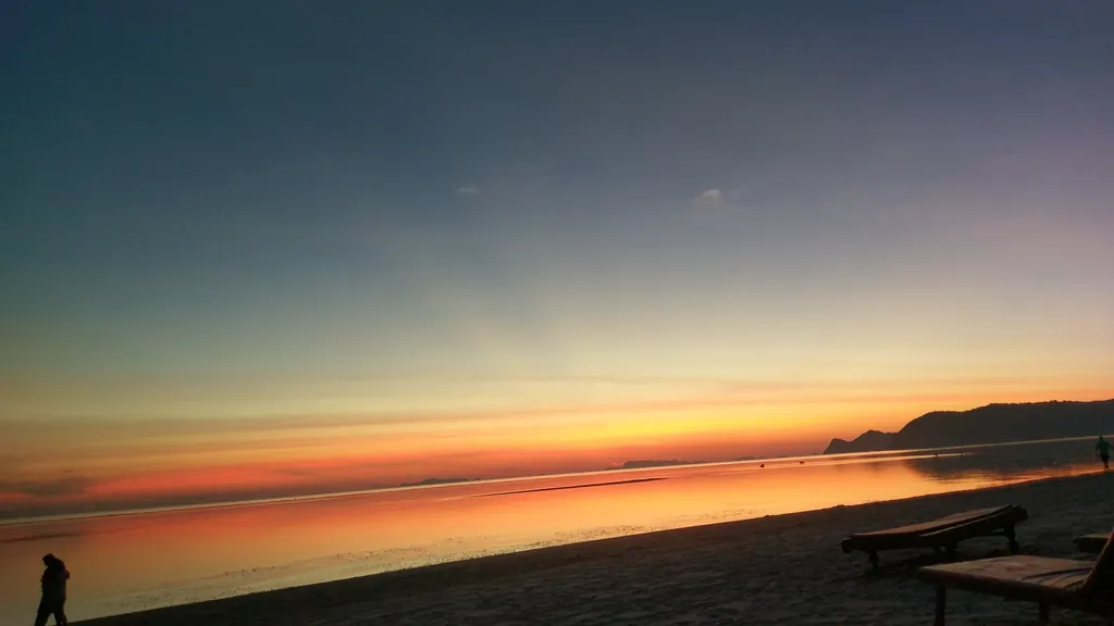 Strand in der Abenddämmerung mit orangem Horizont, am Wasser eine Person